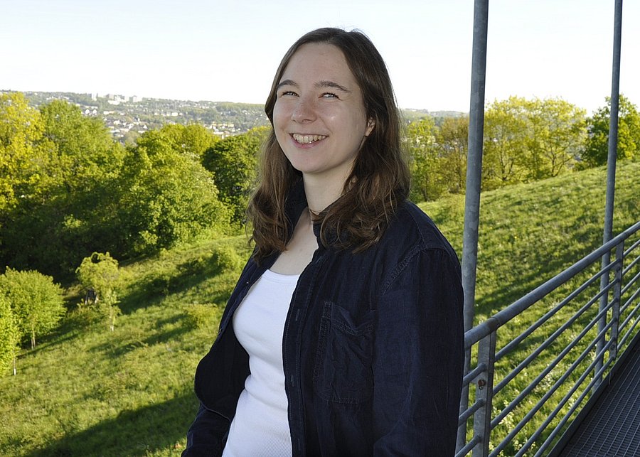 Denise Schmitz steht an der Universität Wuppertal vor der Aussicht auf Wuppertal und lächelt in die Kamera.