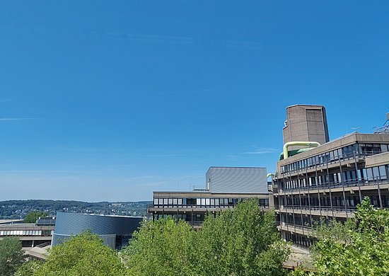 Der Ausblick aus dem Büro zeigt die anderen Universitätsgebäude inkl. der Bibliothek. Es ist strahelnd blauer Himmel.